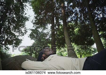 Picture - African man laying in forest. Fotosearch
