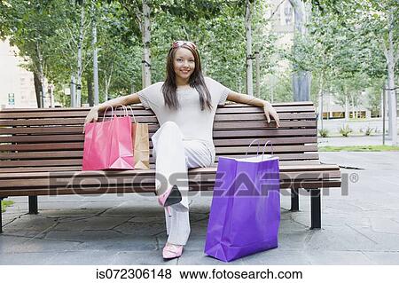 Stock Photo - African woman on park bench with shopping bags. Fotosearch