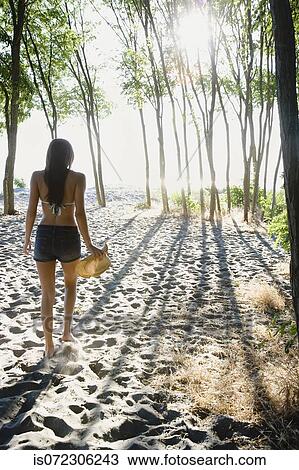 Stock Image - African woman walking on beach with trees. Fotosearch