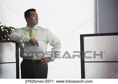Stock Image - Asian businessman leaning on cubicle wall. Fotosearch