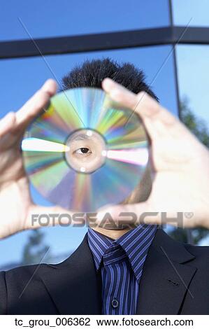 Stock Image - Asian businessman looking through center of cd. Fotosearch