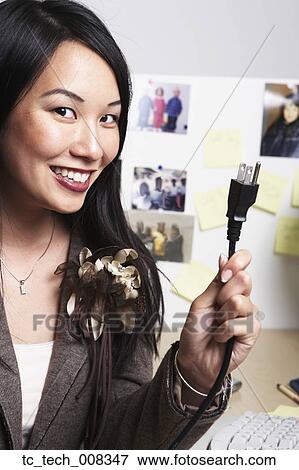 Stock Photo - Asian businesswoman holding up plug. Fotosearch