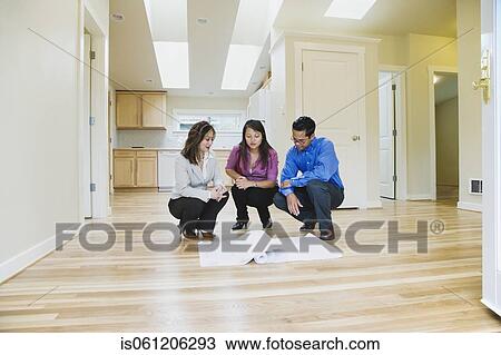 Stock Image - Asian couple looking at blueprints in new house. Fotosearch