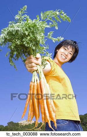 Stock Photo - Asian man holding bunch of carrots. Fotosearch