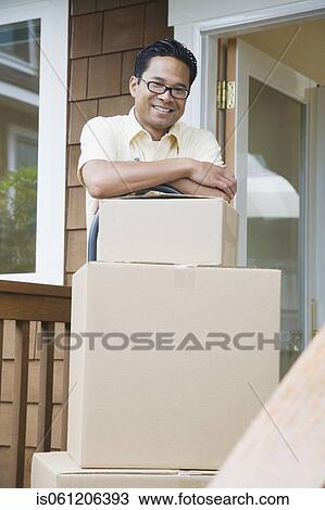 Asian man leaning on moving boxes on porch View Large Photo Image Stock Image - Asian man leaning on moving boxes on porch. Fotosearch