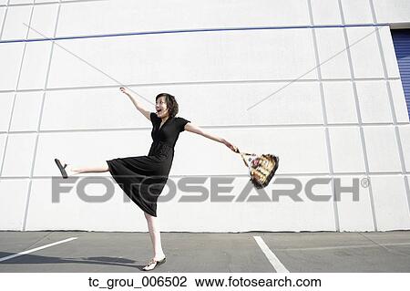 Stock Image - Asian woman kicking up leg in parking lot. Fotosearch
