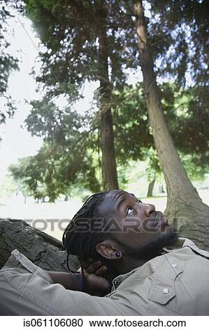 Stock Image - Close up of African man laying in forest. Fotosearch