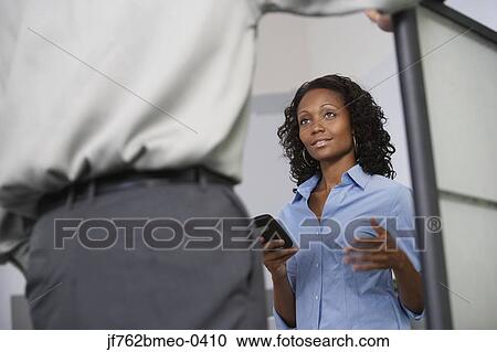 Stock Image - Low angle view of African businesswoman talking to coworker. Fotosearch