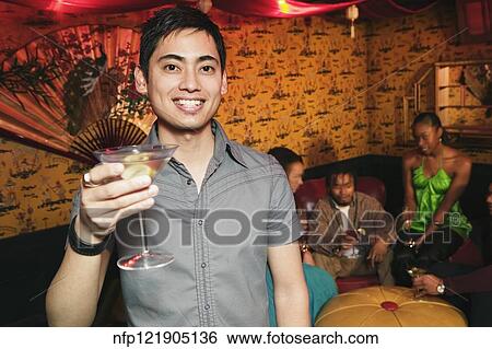 Stock Photograph - Pacific Islander man holding cocktail at nightclub. Fotosearch