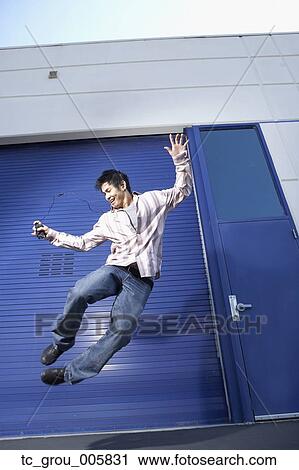 Stock Image - Pacific Islander man listening to mp3 player and jumping. Fotosearch
