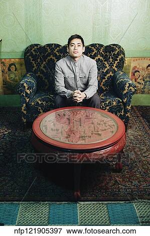 Stock Photo - Pacific Islander man on sofa next to carved table. Fotosearch