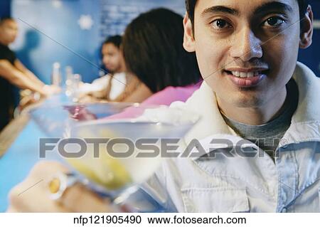 Stock Image - Pacific Islander man toasting with cocktail at bar. Fotosearch