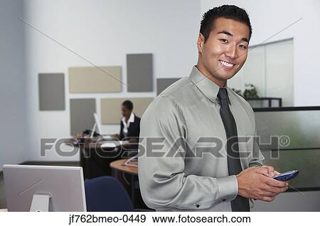 Portrait of Asian businessman holding cell phone View Large Photo Image Stock Photo - Portrait of Asian businessman holding cell phone. Fotosearch