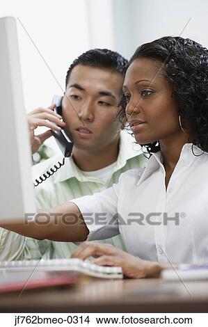 Picture - Two businesspeople working at desk. Fotosearch
