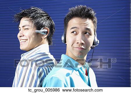 Two young men back to back wearing headsets View Large Photo Image Stock Photograph - Two young men back to back wearing headsets. Fotosearch