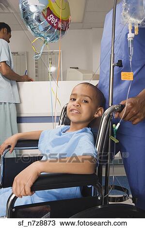 Stock Image - African boy being pushed in wheelchair in hospital. Fotosearch
