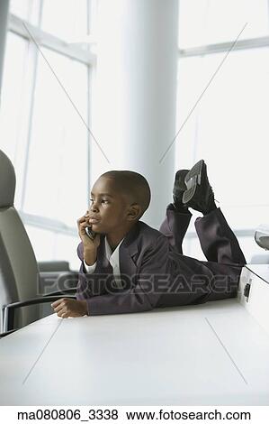 Stock Photo - African boy in business suit laying on table in conference room. Fotosearch