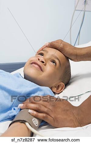 African boy in hospital bed with mother’s hand on forehead View Large Photo Image Stock Photo - African boy in hospital bed with mother’s hand on forehead. Fotosearch