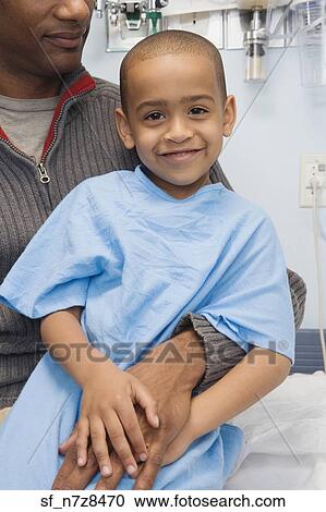 Stock Image - African boy in hospital gown sitting on father’s lap. Fotosearch