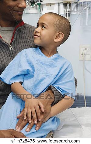 Stock Photography - African boy in hospital gown sitting on father’s lap. Fotosearch