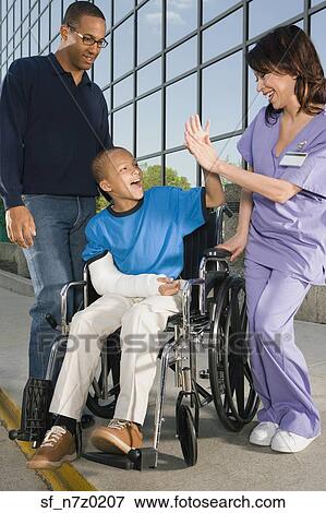 Stock Photo - African boy in wheelchair high-fiving nurse in front of hospital. Fotosearch