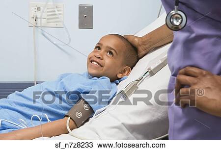 Stock Image - African boy smiling at nurse in hospital bed. Fotosearch