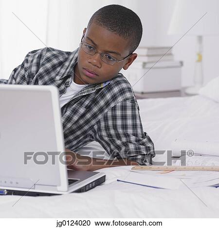 Stock Image - African boy studying with laptop on bed. Fotosearch