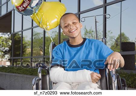 Stock Image - African boy with broken arm and balloons in wheelchair . Fotosearch