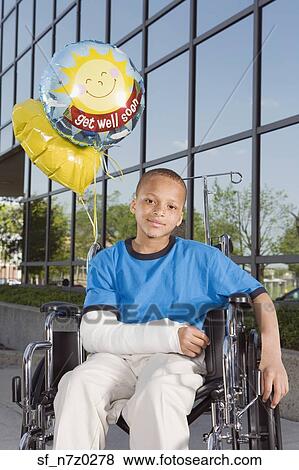Stock Photo - African boy with broken arm and balloons in wheelchair. Fotosearch