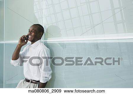 African businessman leaning against wall using cell phone View Large Photo Image Stock Photo - African businessman leaning against wall using cell phone. Fotosearch