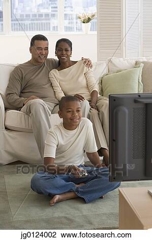 Stock Image - African family watching television in livingroom. Fotosearch
