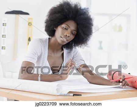 Stock Photo - African female architect looking over blueprints. Fotosearch