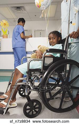 Picture - African girl being pushed in wheelchair in hospital. Fotosearch