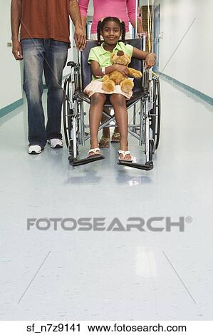 Stock Image - African girl smiling in wheelchair with parents in hospital. Fotosearch