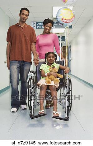 Stock Photography - African girl smiling in wheelchair with parents in hospital. Fotosearch