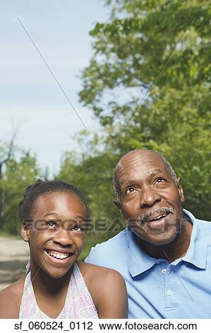 Stock Image - African grandfather and granddaughter looking up in park. Fotosearch