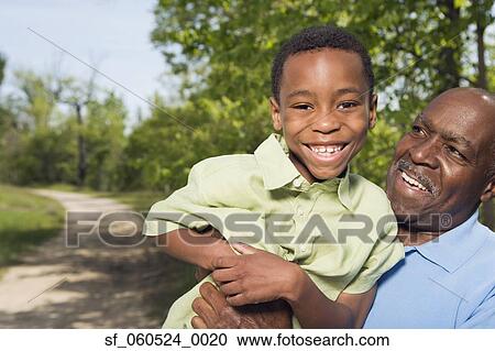 Stock Image - African grandfather holding grandson in park. Fotosearch