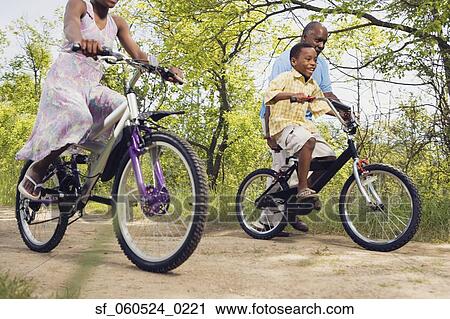 Stock Image - African grandfather teaching grandson to ride a bicycle in park. Fotosearch