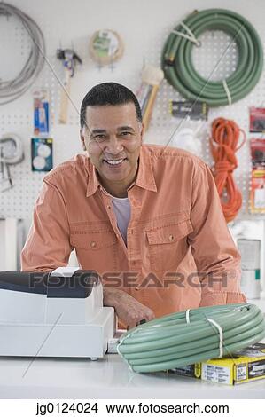 Picture - African hardware store owner smiling behind counter. Fotosearch