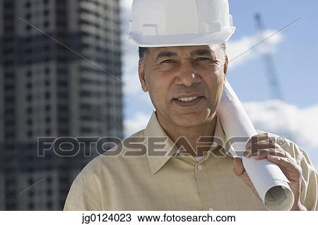 Stock Image - African male contractor with blueprints in urban scene. Fotosearch
