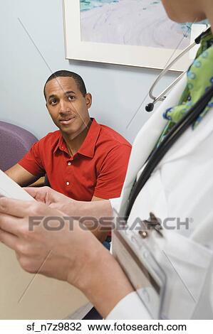 Stock Image - African man talking to doctor in waiting room. Fotosearch