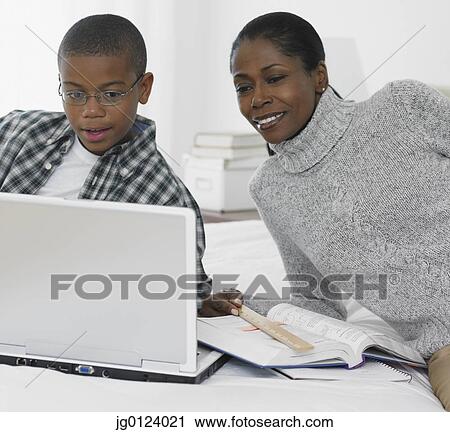 Stock Image - African mother helping son study with laptop. Fotosearch
