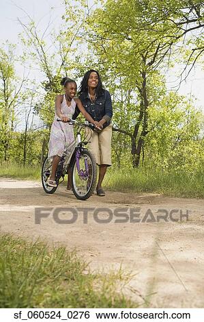 Stock Photograph - African mother teaching daughter to ride a bicycle in park. Fotosearch