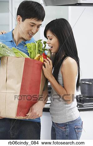 Asian couple looking in grocery bag in kitchen View Large Photo Image Picture - Asian couple looking in grocery bag in kitchen. Fotosearch