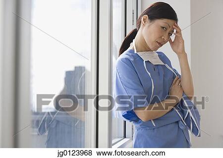 Asian female doctor leaning against window with hand on forehead View Large Photo Image Stock Photo - Asian female doctor leaning against window with hand on forehead. Fotosearch