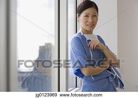 Asian female doctor leaning against window smiling View Large Photo Image Stock Photo - Asian female doctor leaning against window smiling. Fotosearch