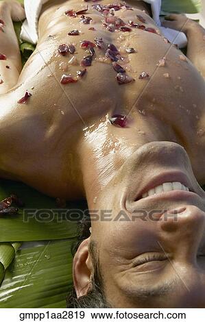 Stock Photo - Asian man laying on banana leaves with crushed fruit on bare chest. Fotosearch