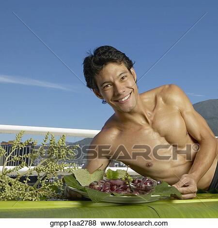 Stock Photo - Bare-chested Asian man laying on banana leaves with fruit platter. Fotosearch