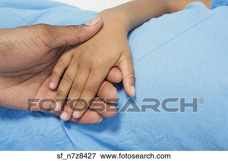 Stock Photo - Close up of African boy holding parent’s hand . Fotosearch