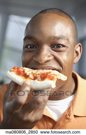Stock Image - Close up of African man eating pizza. Fotosearch